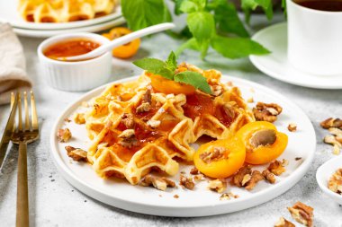 Geleneksel klasik Belçika ya da Brüksel waffleları kayısı reçeli ve açık gri mutfak masasında seramik tabakta ceviz