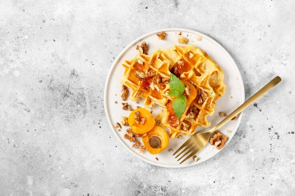 Geleneksel klasik Belçika ya da Brüksel waffle 'ı kayısı reçeli ve açık gri mutfak masasında seramik tabakta ceviz.