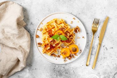 Geleneksel klasik Belçika ya da Brüksel waffle 'ı kayısı reçeli ve açık gri mutfak masasında seramik tabakta ceviz.