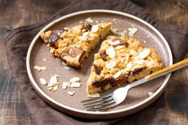 İki parça ev yapımı kurabiye, sütlü, acı çikolatalı ve yakın plan kahverengi bir masadaki bir tabakta badem. Lezzetli tatlı hamur işleri