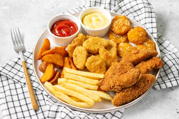 Hafif arkaplanda tavuk nugget, şerit, patates kızartması, kızarmış patates, ketçap ve peynir sosu. Fast food yakın plan.