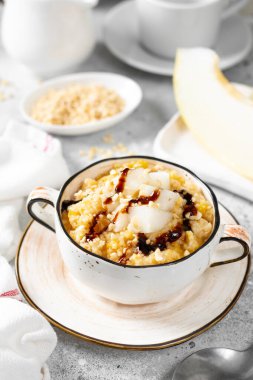 Açık gri mutfak masasında seramik bir kasede kavun dilimleri ve cevizli Millet lapası. Lezzetli ve sağlıklı kahvaltı.