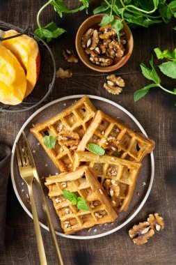 Homemade pumpkin waffles with walnuts in a plate on a brown culinary background top view