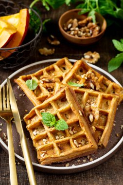 Homemade pumpkin waffles with walnuts in a plate on a brown culinary background closeup