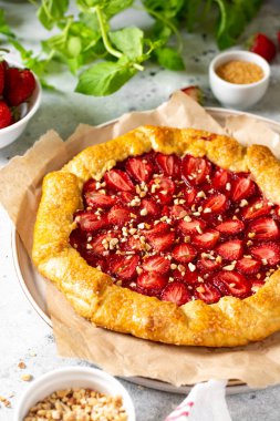Açık gri mutfak arka planında, üzerinde çilek ve badem bulunan Fransız galeti ya da turta. Yaz ev yapımı tatlı hamur işleri