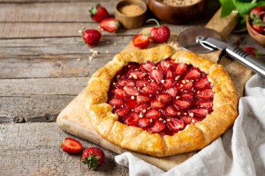 Mutfak arka planında ahşap servis panosunda çilek ve bademli Fransız galeti ya da turta. Yaz ev yapımı tatlı hamur işleri