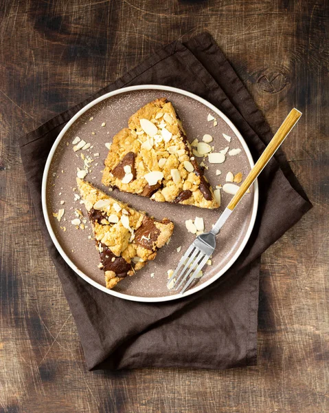 İki parça ev yapımı kurabiye, sütlü, acı çikolatalı ve yakın plan kahverengi bir masadaki bir tabakta badem. Lezzetli tatlı hamur işleri