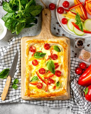 Karışık sebzeli poğaça turtası ve servis tabağında mozzarella peyniri, mutfak masasının üstünde. Domatesli lezzetli hamur işleri, kabak, tatlı biber, baharat ve fesleğen.