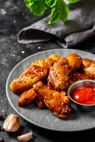 Siyah bir yemek masasında gri bir seramik tabakta barbekü sosunda ev yapımı veya kızarmış tavuk kanadı. Koyu arkaplan