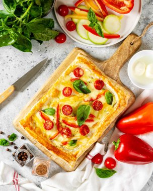 Karışık sebzeli poğaça turtası ve servis tabağında mozzarella peyniri, mutfak masasının üstünde. Domatesli lezzetli hamur işleri, kabak, tatlı biber, baharat ve fesleğen.