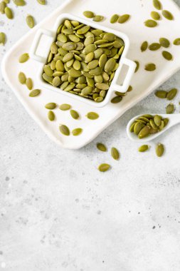 Açık gri bir mutfak arka planında beyaz bir kasede kabak tohumları.