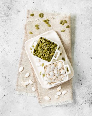 Açık gri mutfak arka planında beyaz bir kasede kabak tohumları.