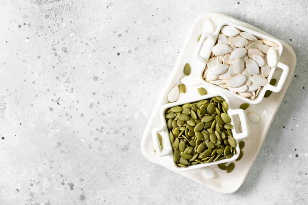 Açık gri mutfak arka planında beyaz bir kasede kabak tohumları.