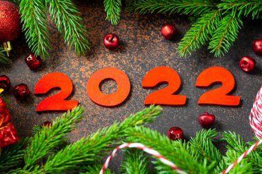 - Mutlu yıllar. Noel ağacının dallarında kırmızı Noel süslemeleri. Ahşap numarası 2022 olan şenlikli bir arka plan.