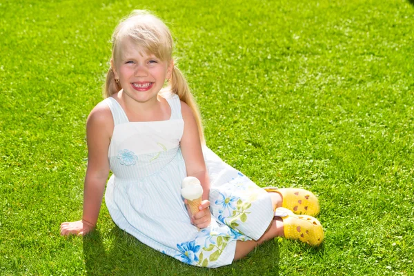Süßes lächelndes kleines Mädchen mit Eis auf dem Gras Stockfoto