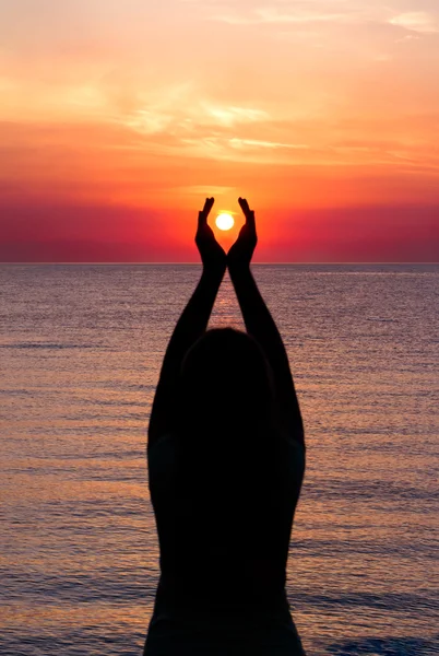 Fille debout sur la plage, regardant coucher de soleil, tenant le soleil dans les mains Photo De Stock