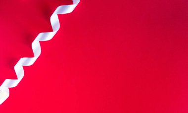 Kırmızı kağıt arka planda minimalist kurdele dekoru var. Karşıtlık ve minimalizm kavramı.