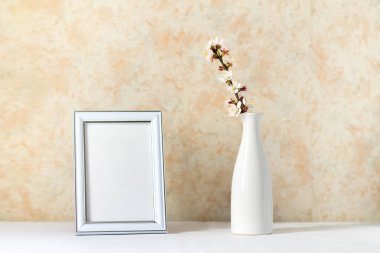 Boş dikey çerçeve beyaz masa üzerinde taklit edilir. Beyaz bir seramik vazoda kayısı dalları açıyor. Sanat konsepti. İskandinav iç tasarımı, insan yok. Bahar hala hayat. 