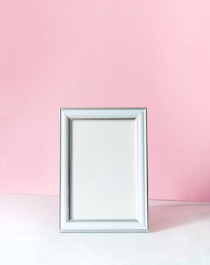 Boş beyaz dikey fotoğraf çerçevesi modeli. Beyaz masa ve pembe duvar arkaplanı. Metin için yeri olan minimalist kavram.