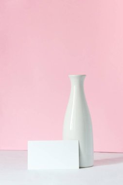 Beyaz bir masada beyaz bir vazo. Arka planda açık pembe bir arka plan var. Metninizi boş bir beyaz karta yerleştirin.