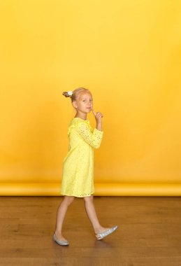 Parlak duyguları olan şirin bir sarışın. Dikkat, gizem, sessizlik, ilgi. O, basit sarı bir elbise giyiyor. Kızın elini kaldırdı, sessizlik ve dikkat göstergesi olarak. Sarı arka plan. Avrupa yarışı.