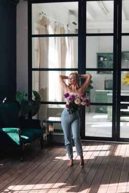 Yıldız çiçekleri olan güzel bir kadın. Pencerenin yanında duruyor. Ellerinizi kaldırın. Dalgın, hayalperest, mutlu yüz. Avrupalı görünümlü, sarışın.