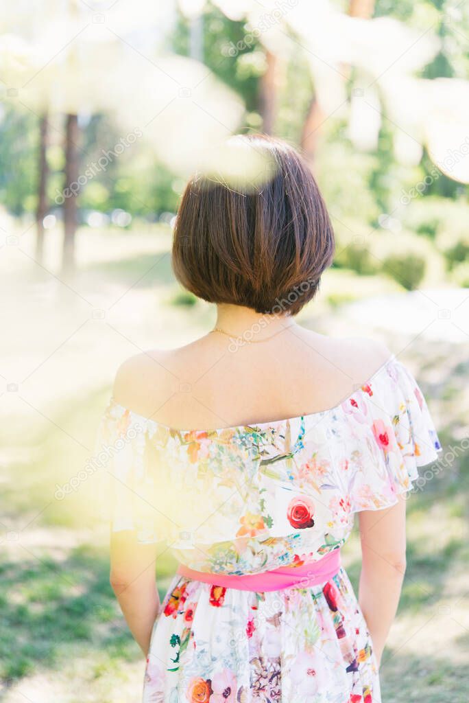 Brunette woman in the park on a sunny summer day. View from the back.