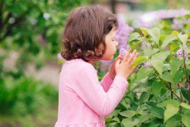 Kız, güneşli bir yaz gününde bahçede çiçek koklar.