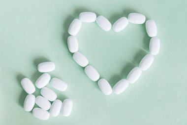 Yeşil arka planda beyaz haplardan yapılmış bir kalp. Sağlık için çeşitli ilaç ve kapsüller, kalp sağlığı ve antiviraller için besin takviyeleri ve vitaminler. Eczacılık..