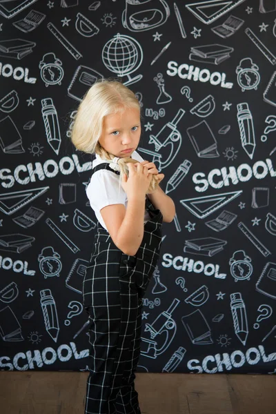 interesting smiling little girl in school clothes against a school board with drawings on the theme of School. Looking at the camera. School concept. Back to school.