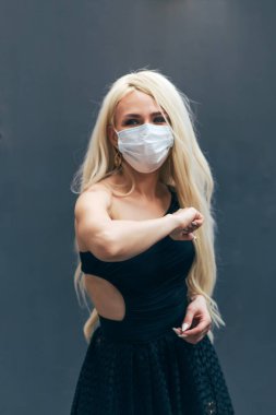 Maskeli bir kadın, seyirciyi dirsekleriyle selamlar, el sıkışmak ya da sarılmak yerine birbirlerini dürterek, covid 19 koronavirüs enfeksiyonunun yayılmasını engeller..