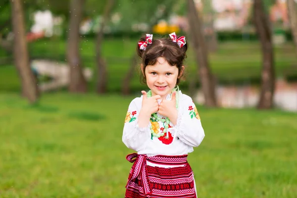 緑の背景にウクライナの民族衣装で楽しい若い女の子の肖像画 屋外だ 笑顔だ 彼の手でサインを見せる — ストック写真