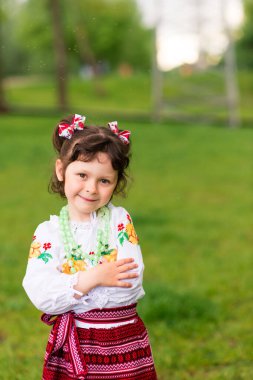 Yeşil arka planda Ukrayna ulusal giysileri içinde neşeli bir genç kızın portresi. Açık havada. Mutlu bir gülümseme Sarılmak için ellerini uzat.