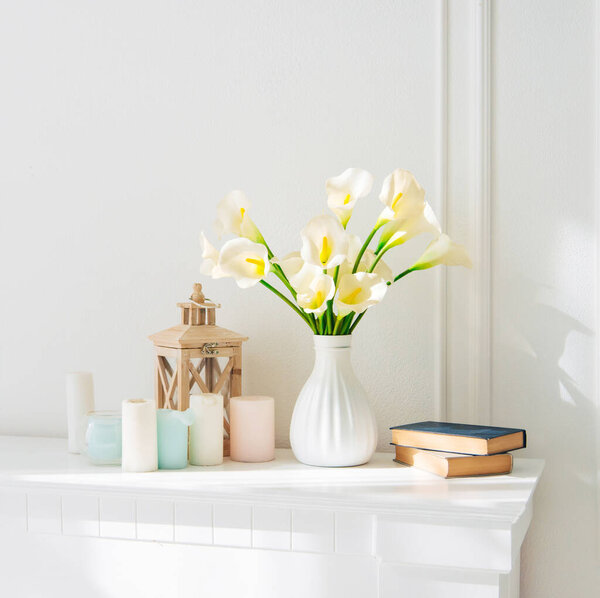 Soft home decor, white jug, vase with white and yellow beautiful flowers on a white wall background and on a wooden shelf. Interior.