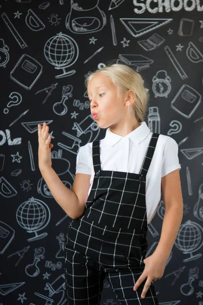 interesting little girl in school clothes against a school board with drawings on the theme of School. School concept. Back to school.