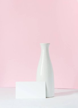 Beyaz bir masada beyaz bir vazo. Arka planda açık pembe bir arka plan var. Metninizi boş bir beyaz karta yerleştirin.