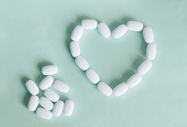 Yeşil arka planda beyaz haplardan yapılmış bir kalp. Sağlık için çeşitli ilaç ve kapsüller, kalp sağlığı ve antiviraller için besin takviyeleri ve vitaminler. Eczacılık..