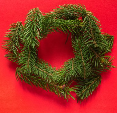 Noel kartı. Kırmızı kağıt arkaplanda köknar dalları çelengi.