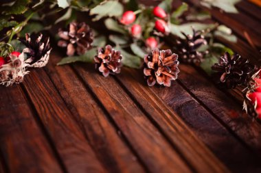 Ahşap arka planda Noel süsü. Külahlar, iğneler, gül kalçalar. Sıcak ve samimi bir kartpostal..