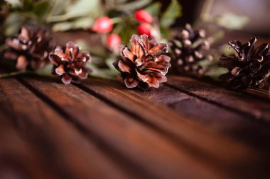 Ahşap arka planda Noel süsü. Külahlar, iğneler, gül kalçalar. Sıcak ve samimi bir kartpostal..