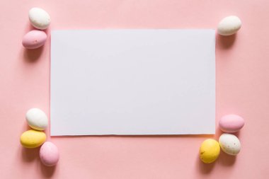 Mutlu Paskalya dekorları. Boş tebrik kartı, davetiye maketi. Şenlikli pastel pembe arka plan, Paskalya yumurtası şeklinde çikolatalar. Boşluğu kopyala, düz yat, üst görünüm.