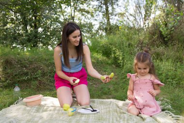 Mutlu anne ve kız piknikte, elma yiyor, parkta çimlerin üzerinde oturuyor, birlikte eğleniyorlar.