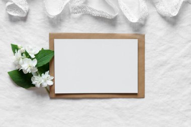 Zarftaki boş kart, beyaz çiçek buketi ve beyaz desenli arka planda şerit, düz yatış. Tebrik kartı modeli