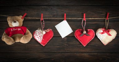 Kırmızı peluş kalpler ve oyuncak ayı bir ipe tutunuyorlar.