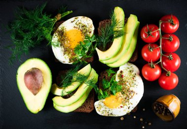 Yumurtalı sağlıklı avokado tostları, siyah arkaplanda domatesler.