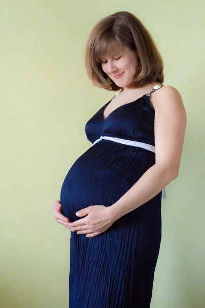 Mulher grávida acariciando sua barriga sobre a parede verde — Fotografia de Stock