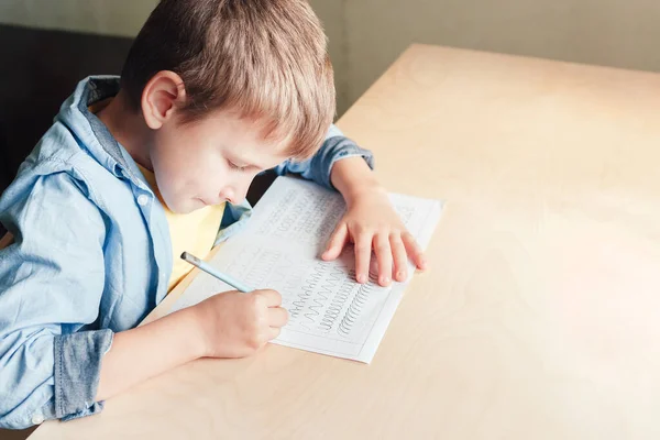 Boy melakukan pekerjaan rumahnya, melacak baris yang berbeda dengan pensil. — Stok Foto