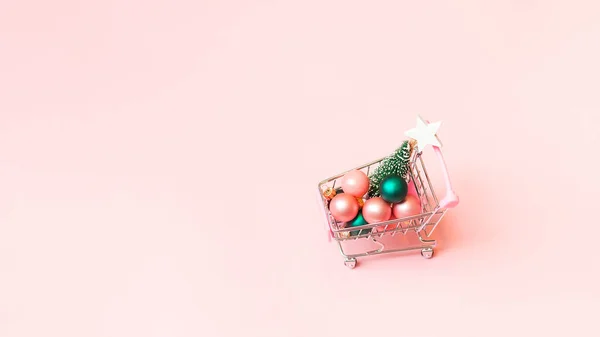 Algunas bolas festivas y árbol de Navidad en miniatura en trolley sobre fondo rosa — Foto de Stock