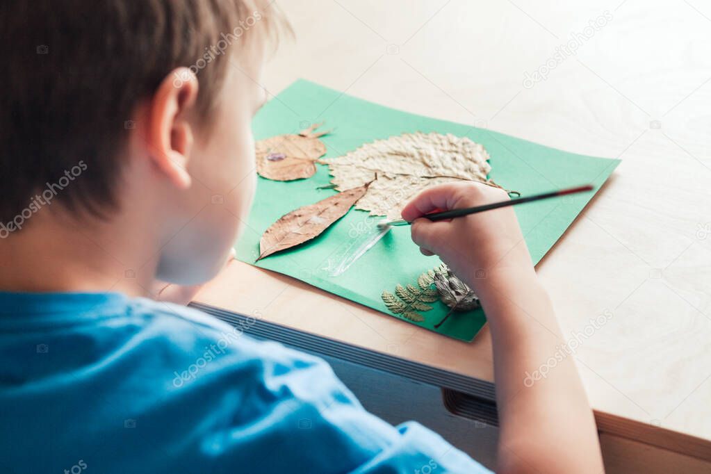 child glues an applique made of autumn leaves