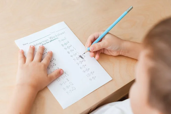 Pandangan atas tangan anak dengan pensil. Menyelesaikan latihan matematika — Stok Foto